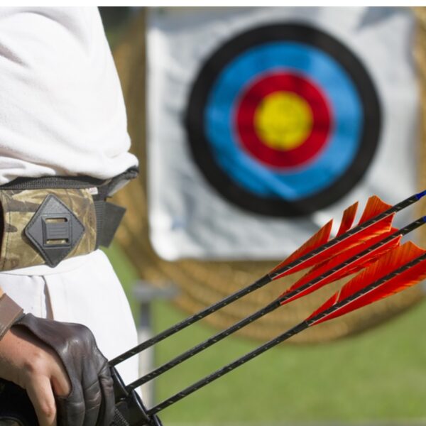 A close up of an Archer holding arrows with the target in the background