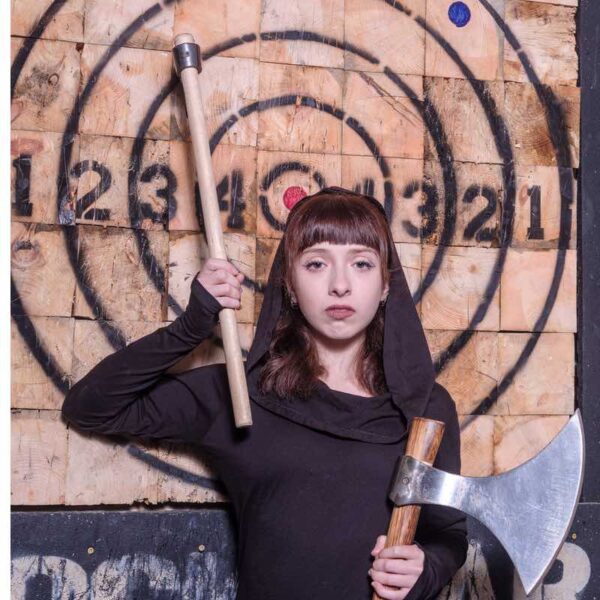 A woman holding an axe posing in front of an Axe Throwing target