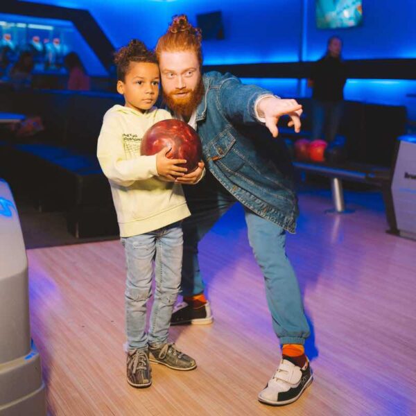 A man coaching his child who is holding a bowling ball