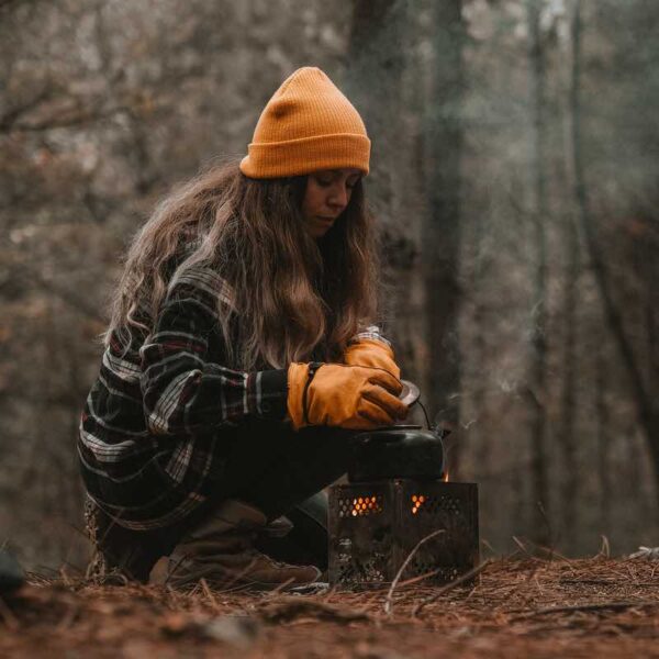 A woman wearing heat resistant gloves boiling a kettle over a manmade fire on a Bushcraft activity.