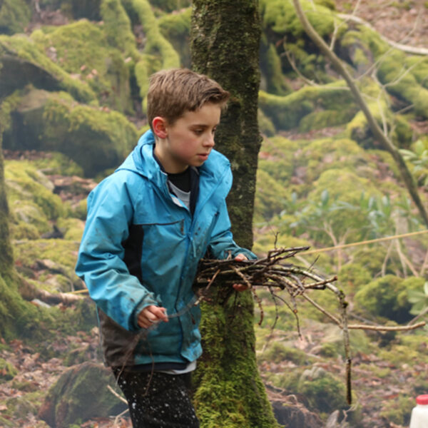 A boy doing a Bushcraft activity in the woods carrying sticks