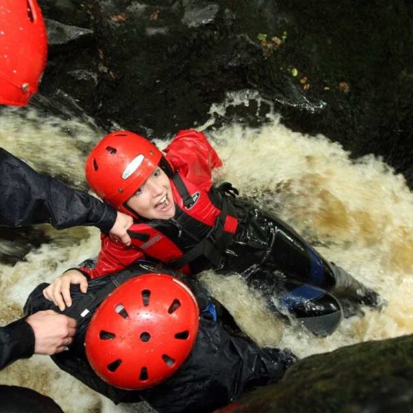 A lady in a wetsuit and red helmet, about to go down a natural rock slide on a Canyoning Gift Experience Day