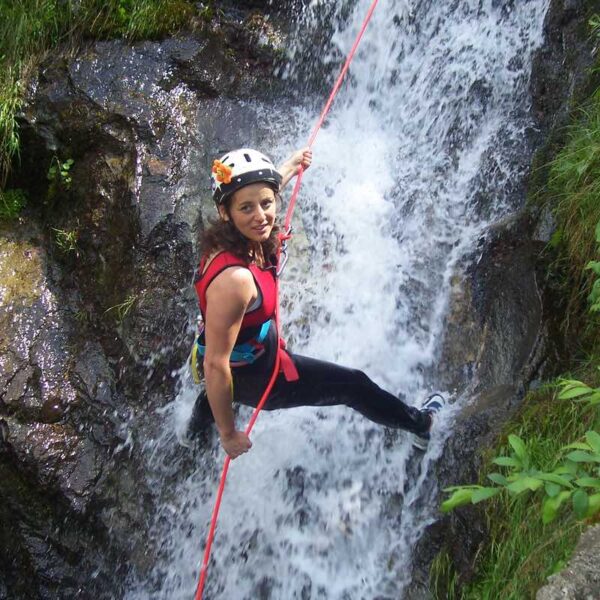 A woman wearing safety gear abseiling down a waterfall for her Canyoning day