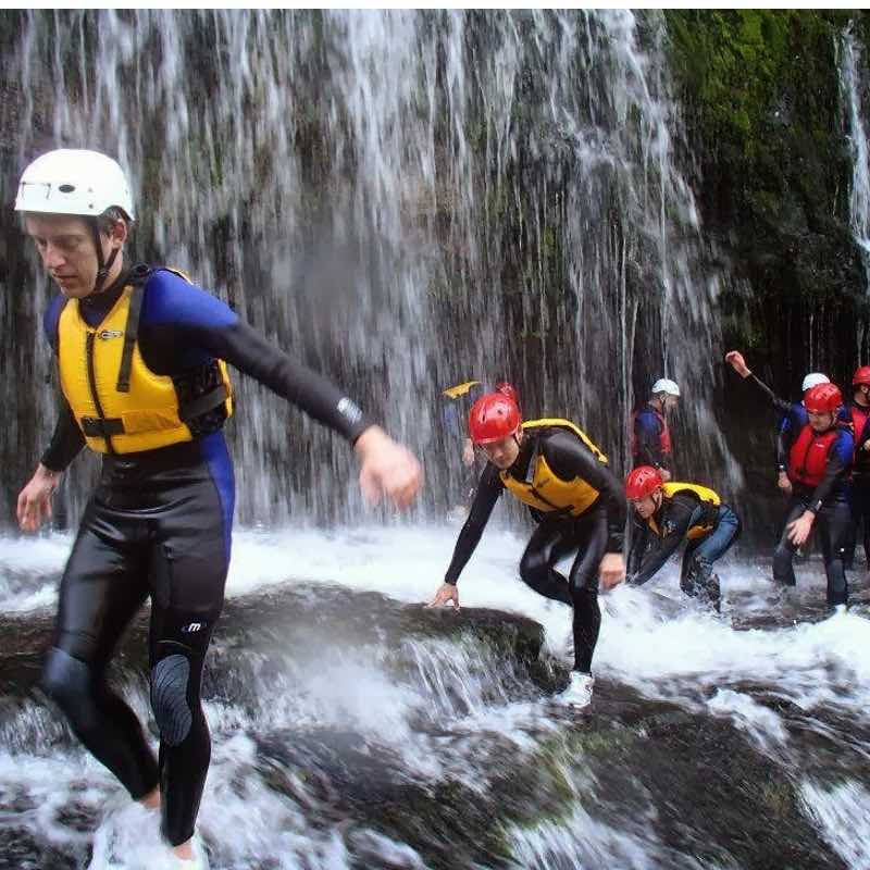 A group dressed in wetsuits and helmets Canyoning under a waterfall