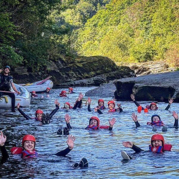 A group wearing helmets floating in water, with their hands in the air during a Canyoning session