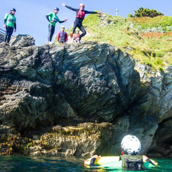 A man dresses in a wetsuit and helmet, jumping off a Cliff into the ocean on a Coasteering Gift Experience Day