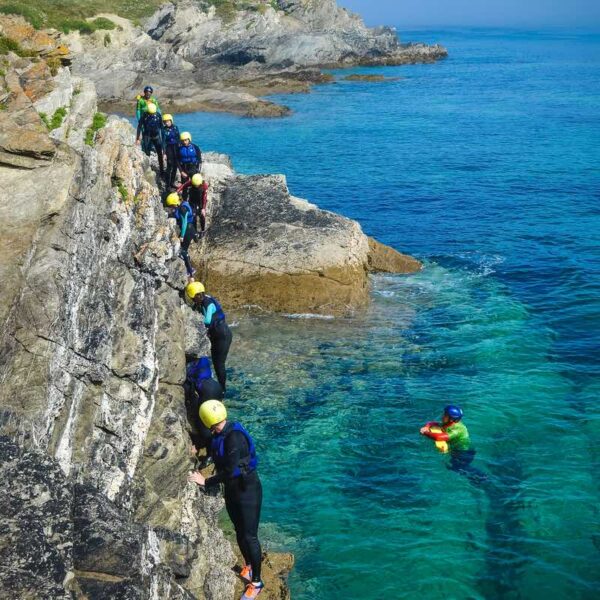 A group wearing wetsuits and helmets Coasteering on a cliff face