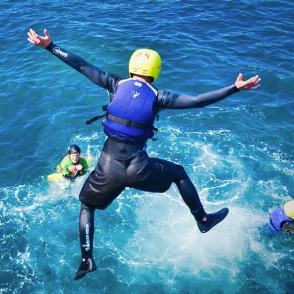 A man wearing a helmet and wetsuit, jumping into the ocean for his Coasteering Gift Experience Day