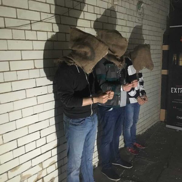 Three people in handcuffs with sacks over their heads in a Horror Escape Room