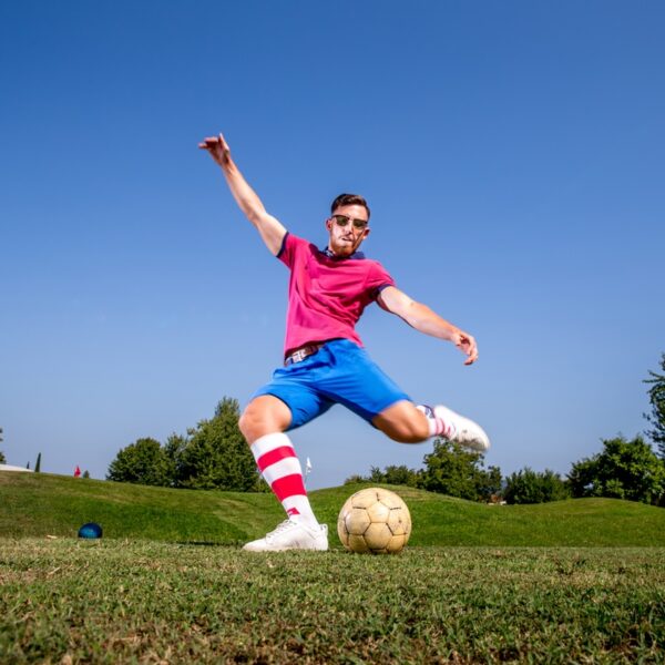 A man wearing football socks, swinging his leg toward a Football playing Footgolf