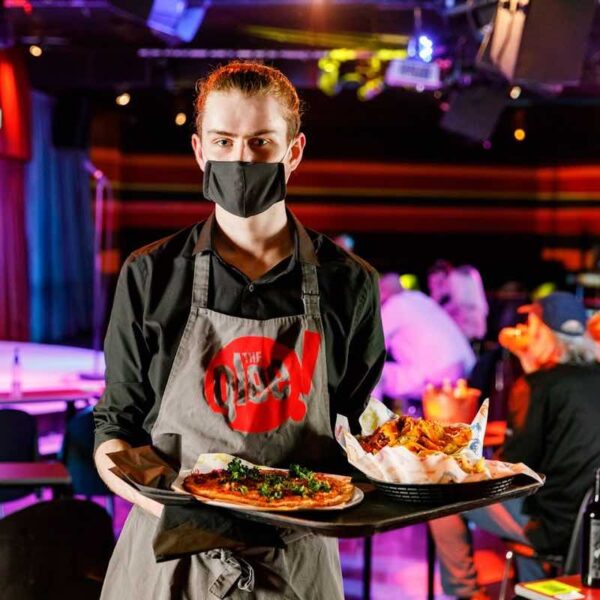 A waiter wearing a Glee Comedy apron holding a tray of food