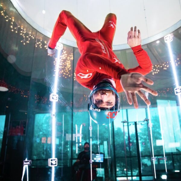 A man upside down wearing a jumpsuit and helmet doing Indoor Skydiving in a Simulator