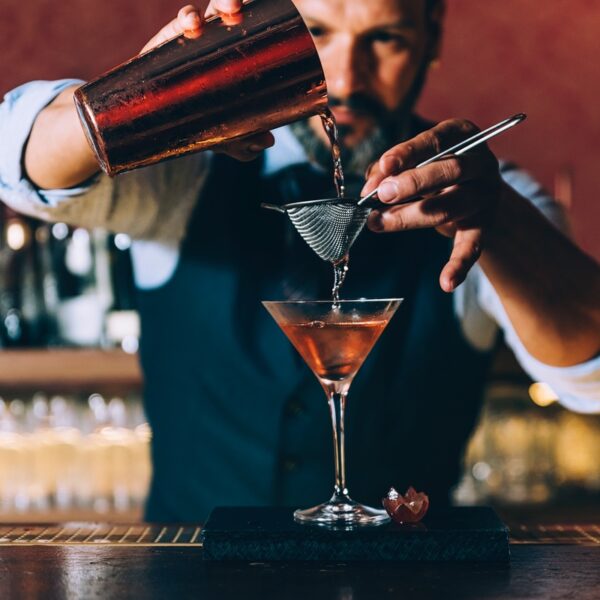 A bartender pouring a Cocktail through a strainer into a glass