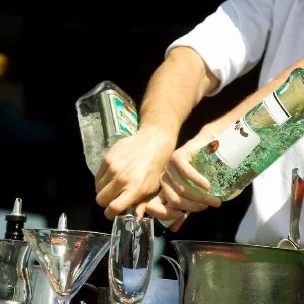 A person pouring 2 bottles of alcohol into a cocktail glass