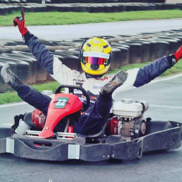 A man dressed in a helmet and jump suit celebrating in an Outdoor Race Kart