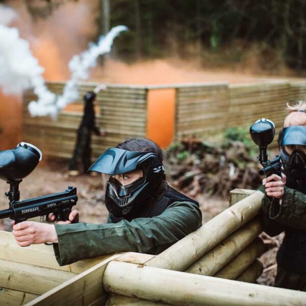 Two girls dressed in overalls and headgear aiming their Paintball guns