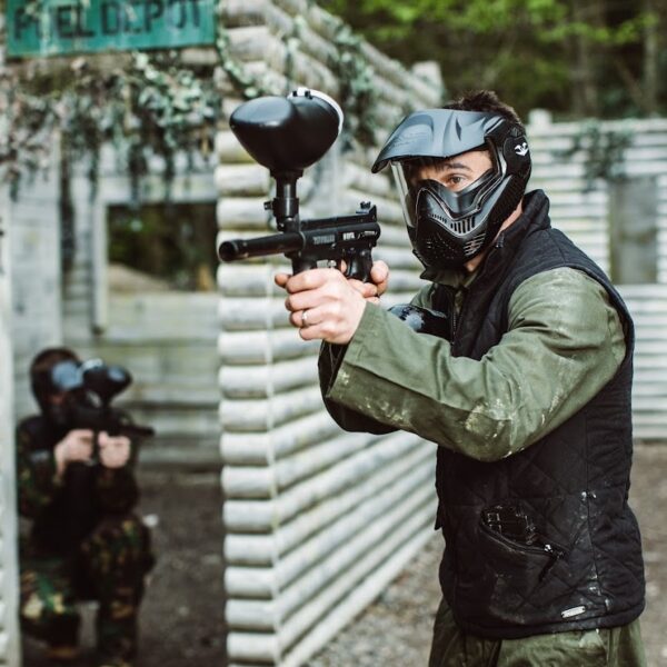 A man playing Paintball, wearing overalls and protective headgear