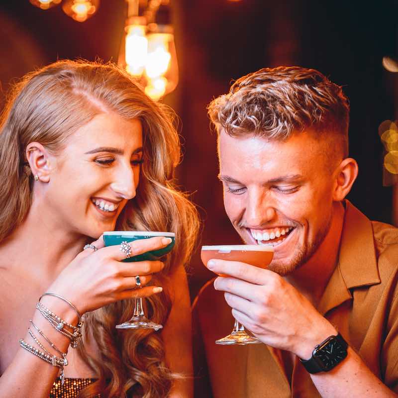 A close up of two people in Revolution smiling about to drink Pornstar martinis