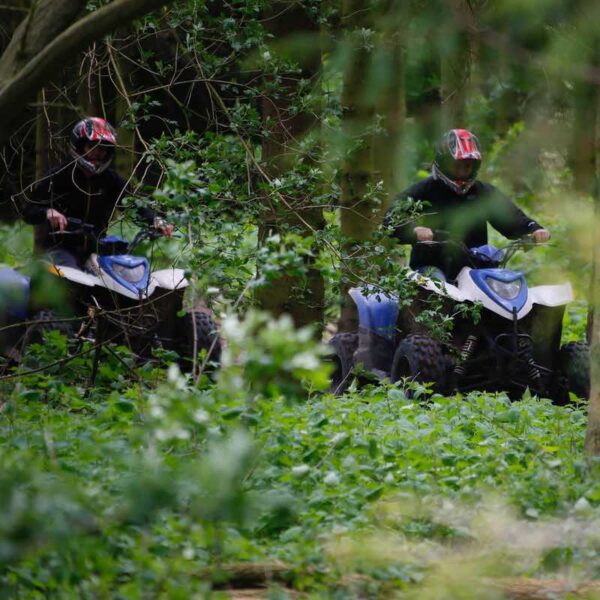 Two people wearing helmets Quad Biking through a forest