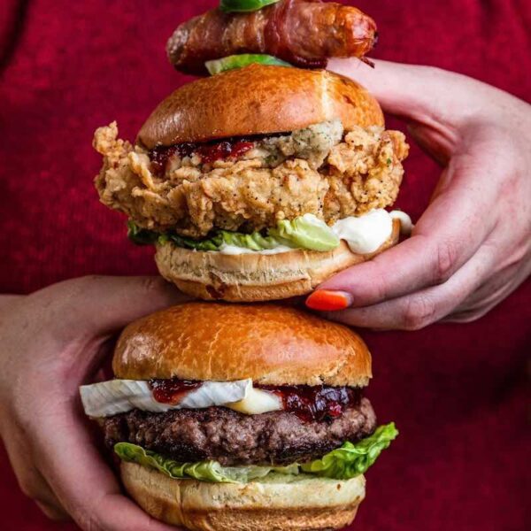 A close up of someone holding two Revolution burgers stacked on top of one another