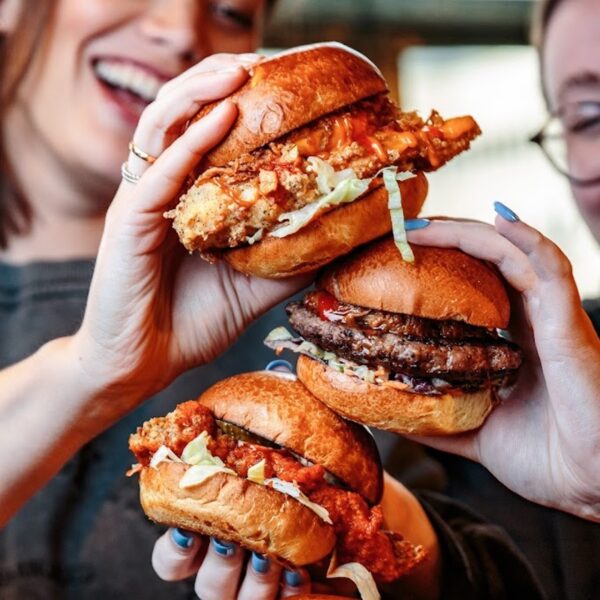 A close up of two women smiling holding different Revolution burgers on top of one another