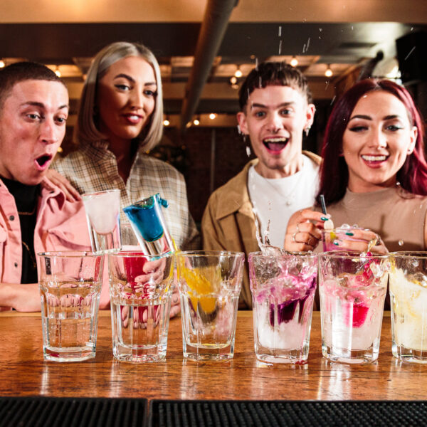 Four people smiling watching shots falling like dominos into cocktails