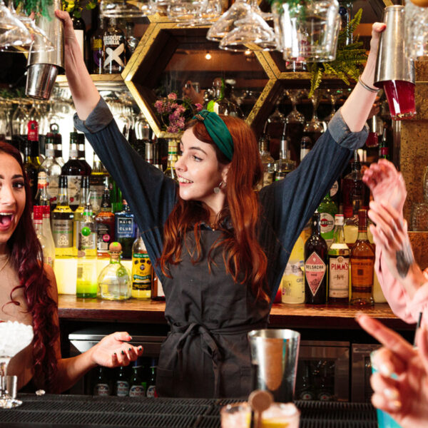 A bartender in a boiler suit holding Cocktail shakers above 2 people's heads
