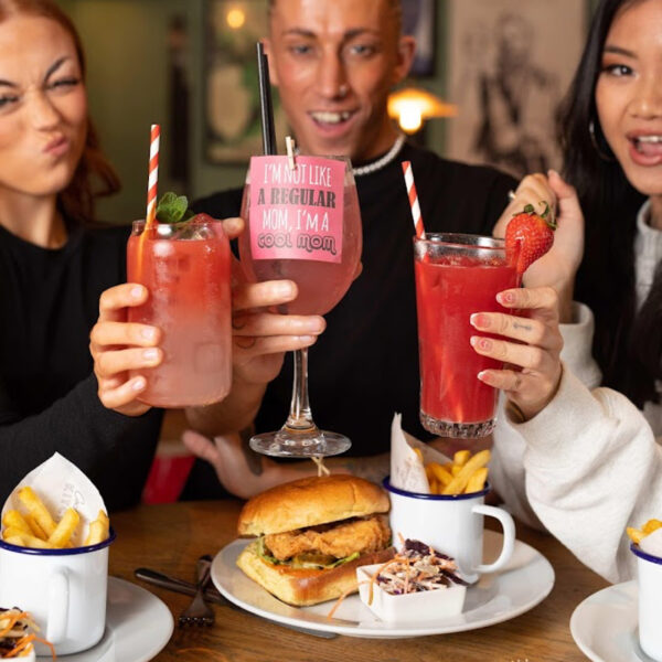 Three people holding Cocktails at a table with burgers and fries