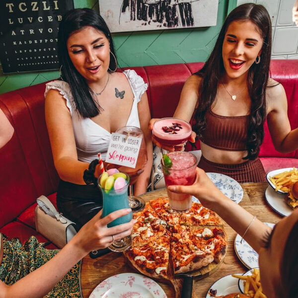 Four girls sat around a table clinking their Cocktails together over a pizza on a gift experience day.