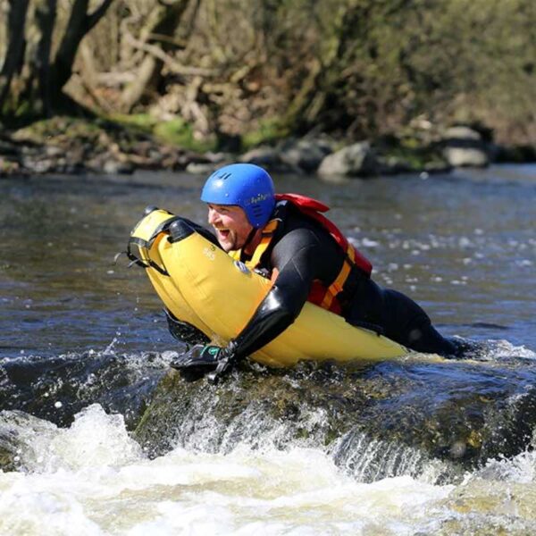 A man dressed in a wetsuit and helmet River Bugging through rapids
