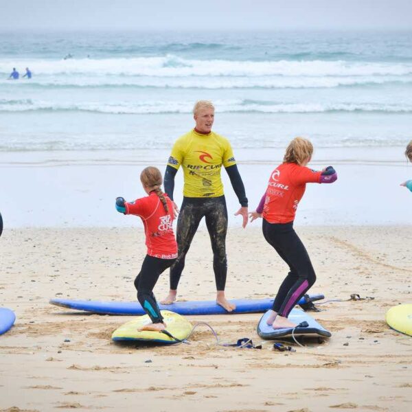 Instructor on a beach teaching 2 kids balancing on surfboards
