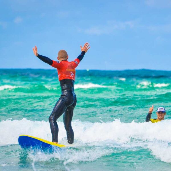 Student surfing in ocean being given a thumbs up by their instructor