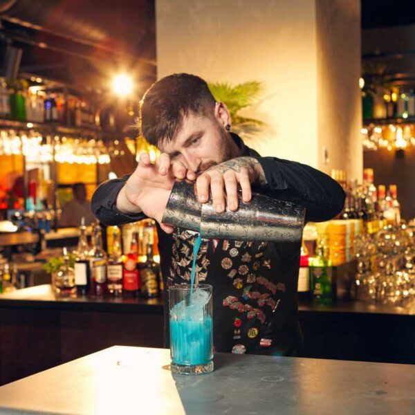 A bartender straining a blue cocktail into a glass on a gift experience day