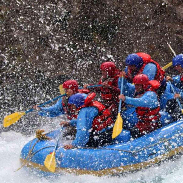 A group splashing their paddles through rapids while White Water Rafting