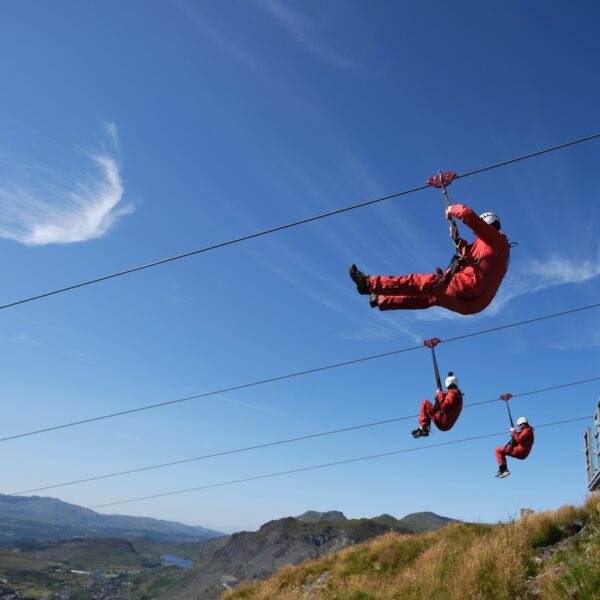 3 people zipping down the Zip Wire Titan dressed in red overalls and helmets