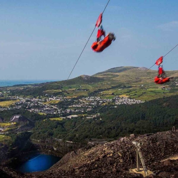 2 people dressed in red overalls flying superman style down the Zip Wire Velocity on a Gift Experience Day